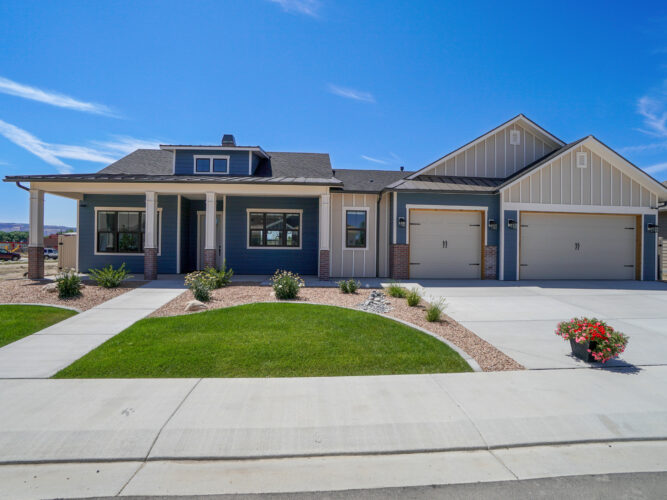 modern landscaped new construction home with blue sky and puffy white clouds. Covered front porch with three car garage