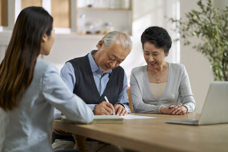 senior asian couple signing an agreement in front of a saleswoman at home